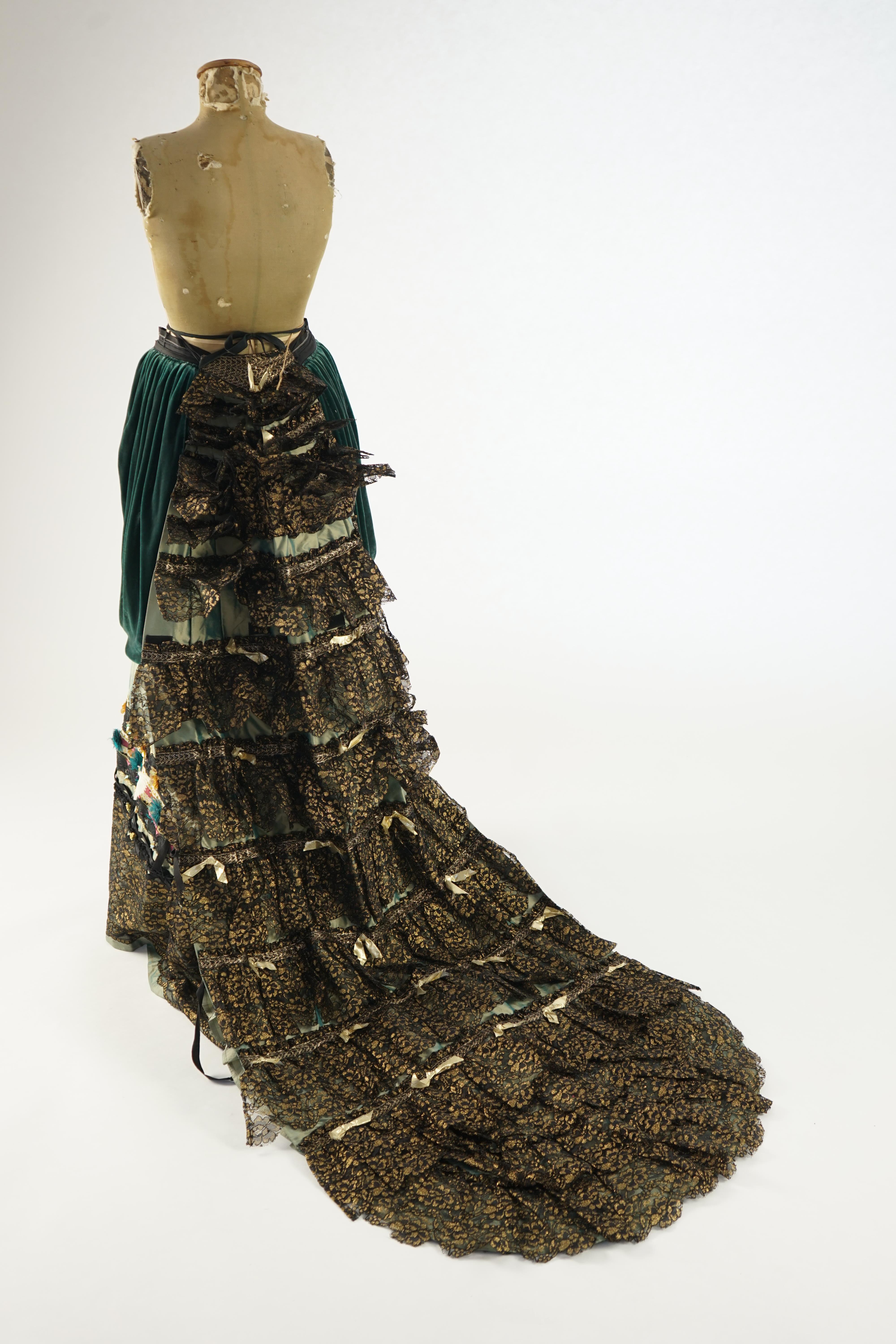 An Edwardian style lady's green taffeta skirt decorated with beaded, sequinned, ribboned border and swags of silk velvet, together with matching train layered with frilled black and gold lace, appliquéd with gold bows